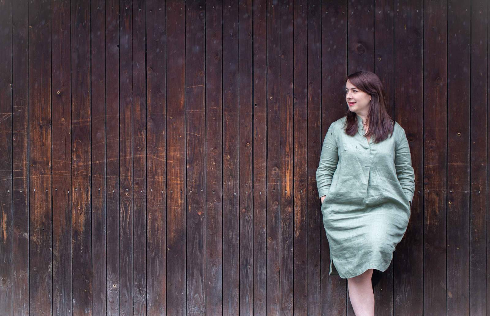 Sandra Fabri lehnt an einer Wand aus Holz.