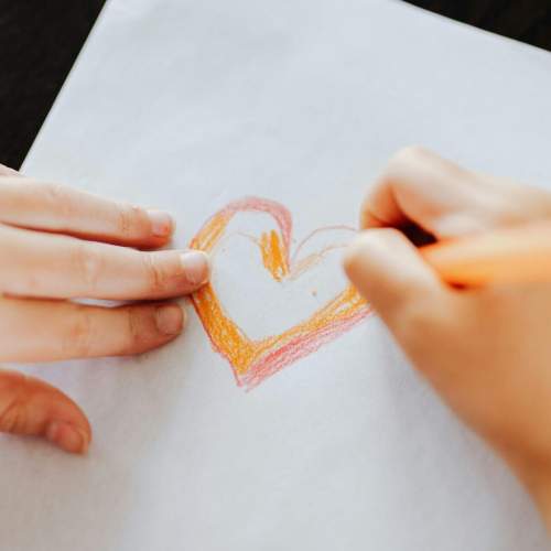 Kind malt mit einem Buntstift ein Herz auf Papier.