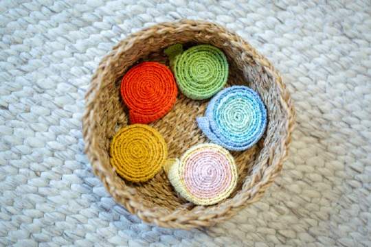 Geflochtener Korb mit aufgerollten gehäkelten Bändern in bunten Farben wie Rot, Grün, Blau, Gelb und Rosa auf Teppich.