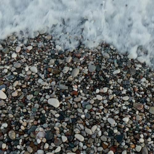 Viele kleine Kieselsteine am Strand mit Wasser.