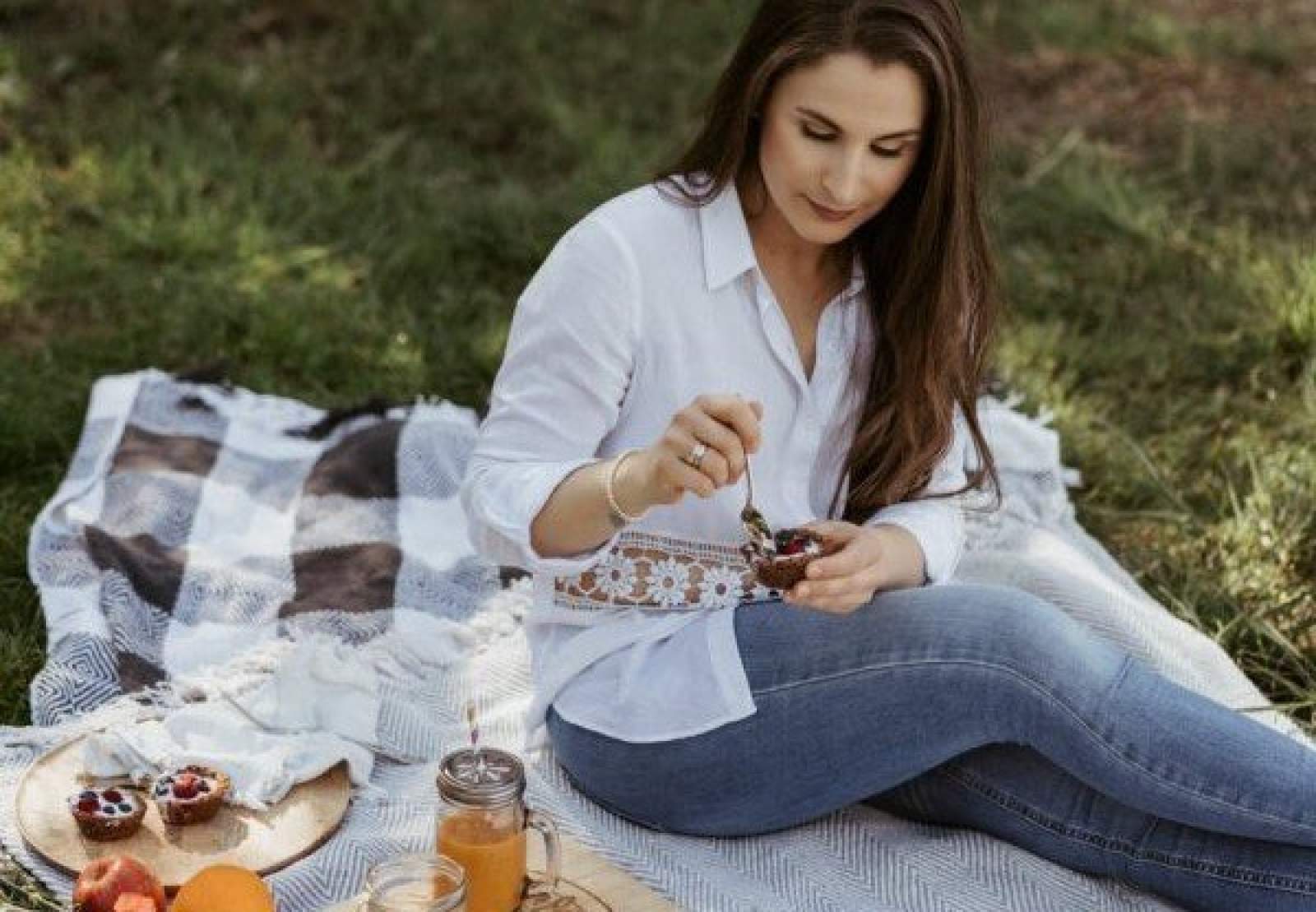Frau sitzt auf einer Picknick Decke und isst ein Dessert.