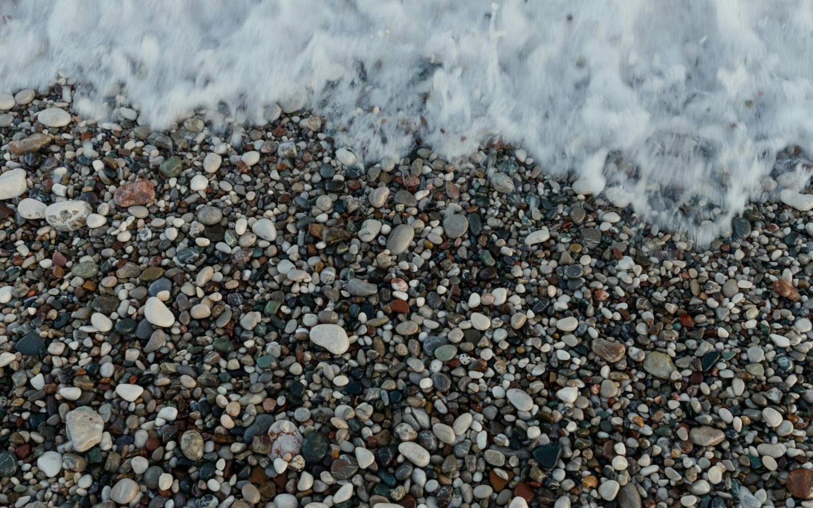 Viele kleine Kieselsteine am Strand mit Wasser.