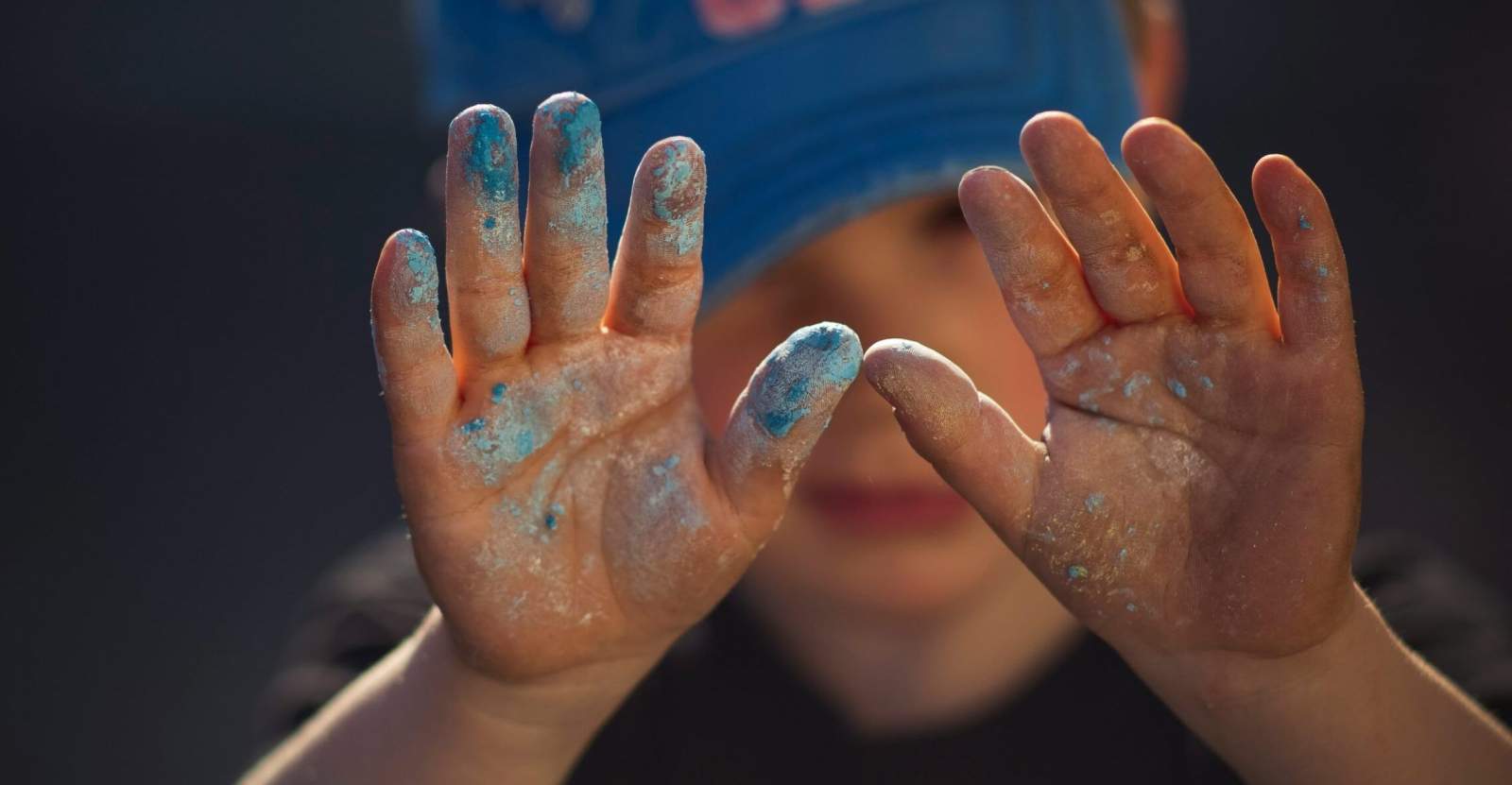 Kleiner Junge mit Farbe an den Händen in blau und gold.