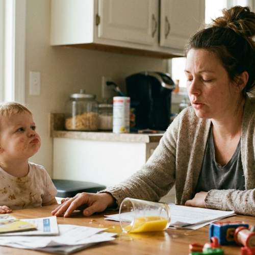 Eine Mutter sitzt mit ihrem Kind an einem chaotischen Tisch.