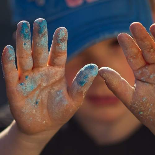 Kleiner Junge mit Farbe an den Händen in blau und gold.