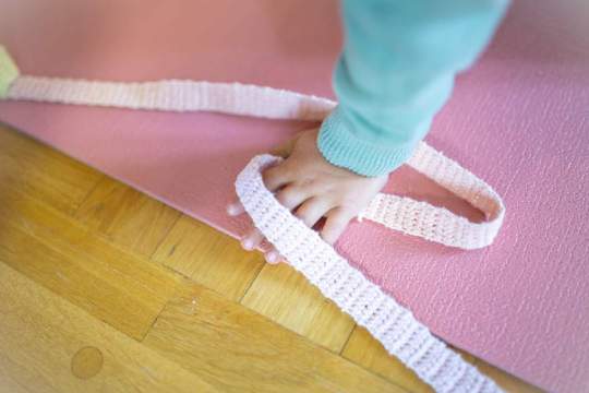 Kinderhand greift nach rosa gehäkeltem Band auf Yogamatte, kreative Beschäftigung mit Handarbeit und Häkeln.