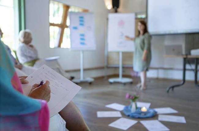 Astrologie-Seminar zur Kinderastrologie mit Flipchart-Präsentation, Teilnehmer machen sich Notizen während die Astrologin die Bedeutung von Sternzeichen für Kinder erklärt.