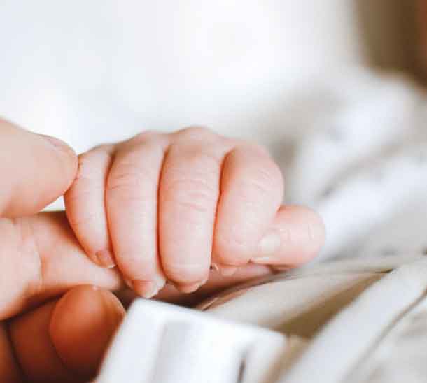 Das Bild zeigt ein Baby das eine Hand hält und soll symbolisieren, welche sinnvollen Geschenkideen es zur Geburt gibt